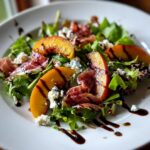 A vibrant Grilled Peach Prosciutto Salad featuring grilled peach slices, prosciutto, crumbled cheese, and greens drizzled with balsamic glaze.