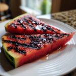 Close-up of two juicy Grilled Watermelon Wedges served on a white plate, showing distinct dark grill marks.