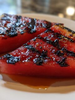 Close-up of two glistening, caramelized Grilled Watermelon Wedges with distinct grill marks on a white plate.
