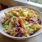 A bowl filled with vibrant Hawaiian Pineapple Coleslaw featuring shredded cabbage, carrots, pineapple chunks, and green onions in a creamy dressing.