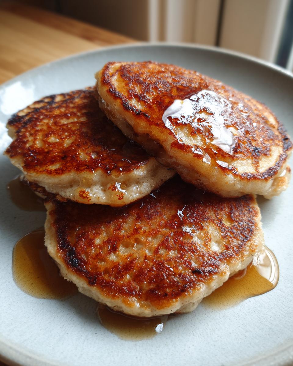 Close-up of a stack of three golden-brown Healthy Banana Pancakes drizzled with maple syrup on a light gray plate.