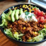 A close-up view of a colorful Healthy Turkey Taco Bowl filled with seasoned ground turkey, lettuce, avocado, corn, black beans, and sour cream.