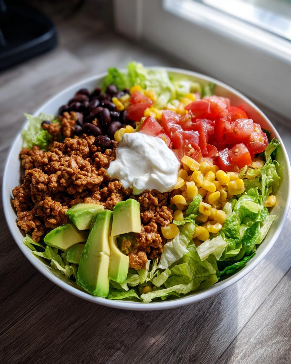 A vibrant bowl featuring ground turkey, avocado, black beans, corn, tomatoes, lettuce, and sour cream for a Healthy Turkey Taco Bowl.