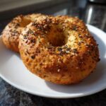 Two golden brown Homemade Gluten Free Protein Bagels topped with everything bagel seasoning on a white plate.