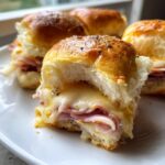 Close-up of a Hot Ham And Cheese Slider with a bite taken out, showing melted cheese and ham.