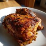 Close-up of two perfectly cooked Juicy Slow Cooker Chicken Thighs with a rich, browned, seasoned crust on a white plate.
