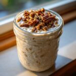 Close-up of Maple Pecan Overnight Oats topped with candied pecans in a glass jar.