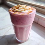 A tall glass filled with a pink Maple Strawberry Milkshake, topped with whipped cream and a caramel drizzle.