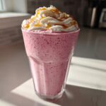 A tall glass filled with a pink Maple Strawberry Milkshake, topped with whipped cream and caramel drizzle.