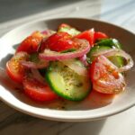 Close-up of Marinated Cucumbers Onions And Tomatoes salad, glistening with dressing and sprinkled with herbs.