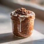 Close-up of rich Mocha Overnight Oats in a glass jar topped with white drizzle and chocolate crumbles.