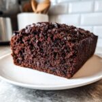 A close-up view of a moist slice of dark Chocolate Zucchini Bread on a white plate.