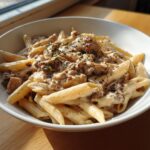 A close-up of a white bowl filled with One Pot Creamy Cajun Chicken Pasta, garnished with herbs and spices.