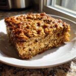 A square slice of moist Peanut Butter Banana Oatmeal Bake with a glossy, baked oat topping.