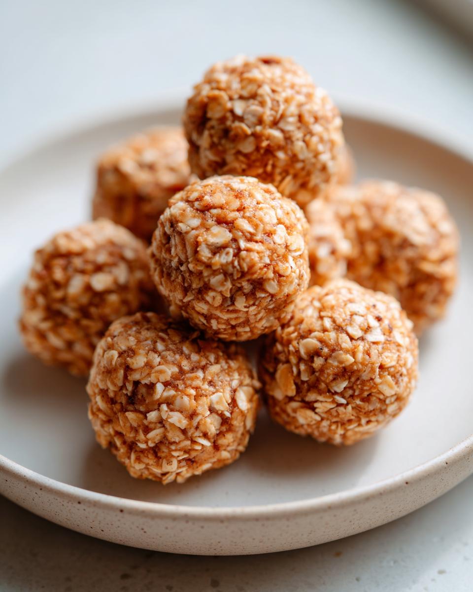 A close-up stack of golden Peanut Butter Protein Balls coated in visible rolled oats, resting on a light ceramic plate.