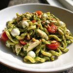 Close-up of Pesto Chicken Pasta Salad featuring twisted pasta, chunks of chicken, cherry tomatoes, mozzarella balls, and pine nuts.