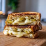 Close-up of a Pickle Grilled Cheese Sandwich cut in half, showing melted cheese oozing over pickle slices.