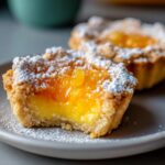 Close-up of a Pineapple Jalapeno Curd Tartlet with a bite taken out, showing the bright yellow curd and topping, dusted with powdered sugar.