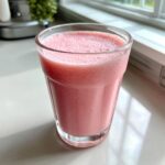A close-up of a frothy, bright pink cloud smoothie served in a clear glass on a light countertop.