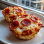 Two golden-brown Pizza Cupcakes topped with melted mozzarella cheese and crispy pepperoni slices on a white plate.