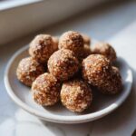 A close-up of several homemade Peanut Butter Protein Balls coated in oats, stacked on a small white plate.