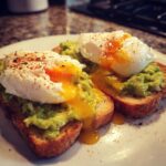 Two slices of Potato Avocado Toast With Perfectly Poached Eggs, showing runny yolk spilling onto the plate.