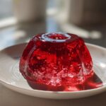 A glistening, molded, bright red Protein Jello Delight sitting on a small white dessert plate.