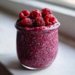 Close-up of Raspberry Chia Pudding Sweetened With Maple Syrup, topped with fresh raspberries, in a glass jar.