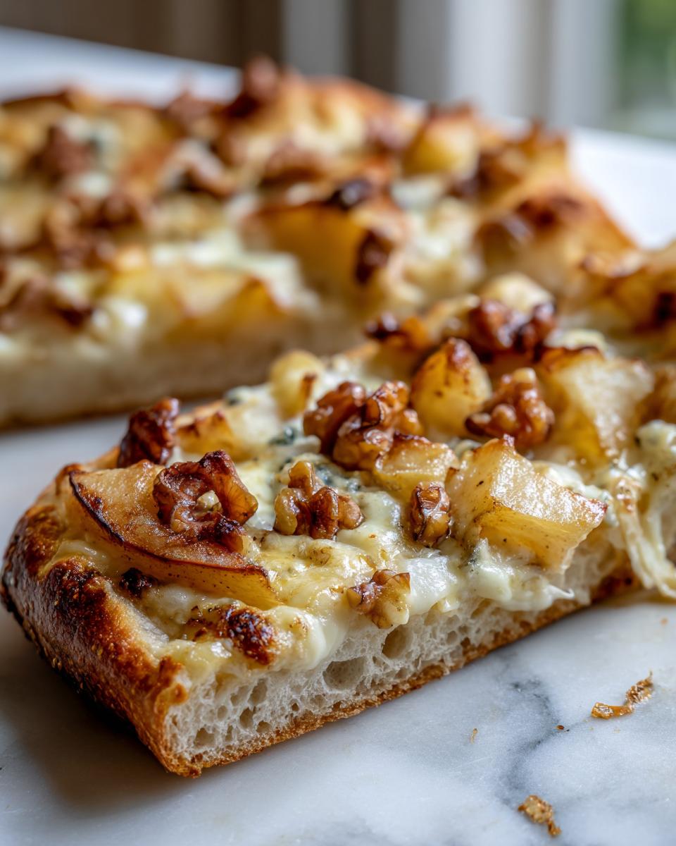 Close-up of a slice of Roasted Pear Flatbread With Gorgonzola showing melted cheese, walnuts, and pear on a thick crust.