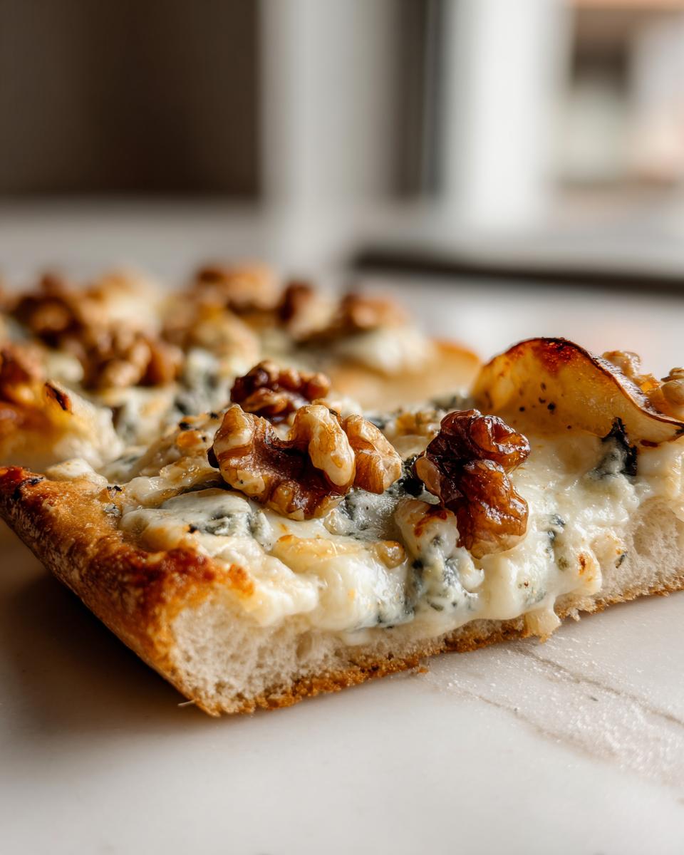Close-up of a slice of Roasted Pear Flatbread With Gorgonzola, topped with walnuts and melted cheese.