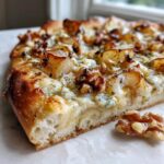 Close-up of a slice of Roasted Pear Flatbread With Gorgonzola, topped with cheese, walnuts, and roasted pears.
