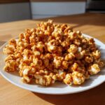 A generous pile of glossy, homemade Salted Caramel Popcorn coated in rich caramel sauce on a white plate.