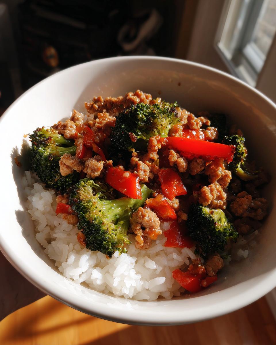 Close-up of a Sauteed Sausage Veggie Rice Bowl topped with ground sausage, bright green broccoli, and red bell peppers over white rice.
