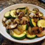 A close-up of Sauteed Zucchini With Mushrooms And Onion served in a white bowl.