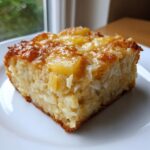 A close-up of a moist slice of Pineapple Casserole featuring visible chunks of pineapple and a golden, caramelized top.