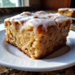 A close-up of a square portion of Soft Chewy Apple Blondies With Maple Glaze, drizzled with white icing, sitting on a white plate.