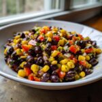 A close-up of a vibrant Southwest Black Bean Salad featuring black beans, corn, diced red peppers, and herbs in a white bowl.
