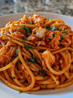 A close-up serving of Spicy Crab Linguettine tossed in a red sauce and topped with fresh parsley.