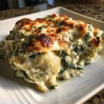 A close-up serving of creamy Spinach Artichoke Ravioli Bake with a bubbly, browned cheese topping.