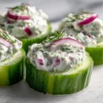 Close-up of fresh Stuffed Cucumber Bites topped with creamy dill filling, red onion, and dill sprigs.