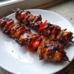 Two skewers of glossy, caramelized Teriyaki Grilled Chicken Kabobs with charred red peppers and onions on a white plate.
