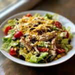 A close-up of a vibrant Tex Mex Chopped Chicken Salad featuring shredded chicken, lettuce, corn, black beans, tomatoes, and shredded cheese.