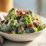 Close-up of The Best Broccoli Salad in a light bowl, featuring creamy dressing, bacon, and raisins.