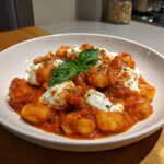 A close-up of rich Tomato Basil Gnocchi With Burrata covered in vibrant red sauce and topped with fresh basil.