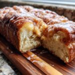A close-up of a freshly baked Apple Fritter Pull Apart Bread loaf, drizzled with white icing, resting on a wooden board.
