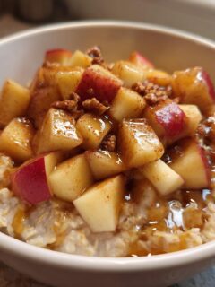Close-up of a white bowl filled with Apple Pie Breakfast Bowl 3, topped with diced, cinnamon-spiced apples and syrup.