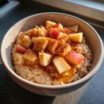 Close-up of a warm Apple Pie Breakfast Bowl topped with diced red apples, cinnamon, and syrup.