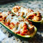 Close-up of two Chicken Parmesan Zucchini Boats topped with melted, slightly browned mozzarella cheese.