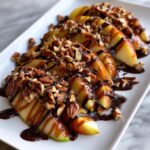 Close-up of fresh apple slices topped generously with chocolate sauce, caramel, and chopped pecans for Chocolate Turtle Apple Slices.
