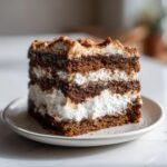 A close-up of a layered slice of Gingersnap Icebox Cake showing dark gingersnap layers alternating with thick white cream filling.